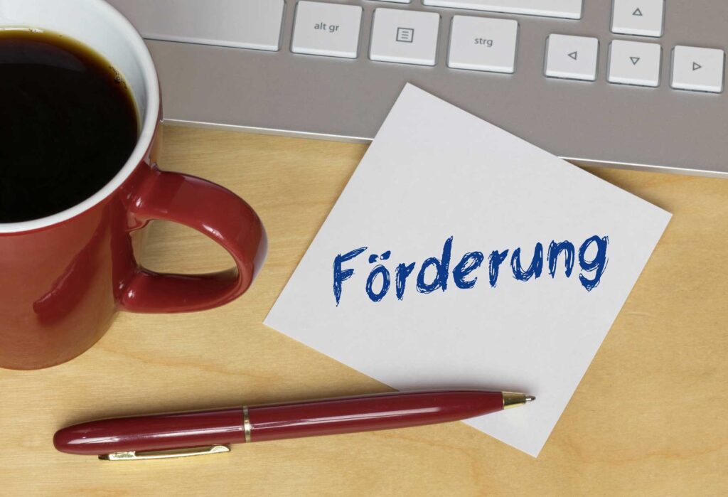 Schreibtisch mit Kaffe und Zettel auf dem Förderung steht