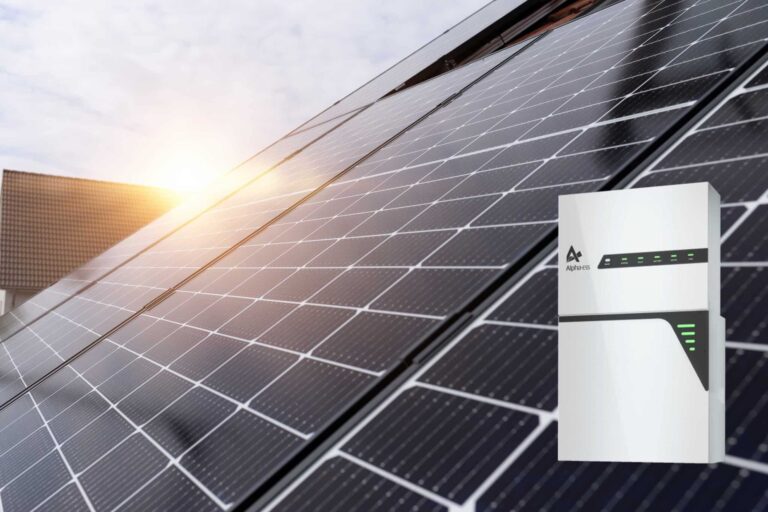 Alpha Batteriespeicher in Weiß zu sehen und dahinter Hausdach mit Solarmodulen.