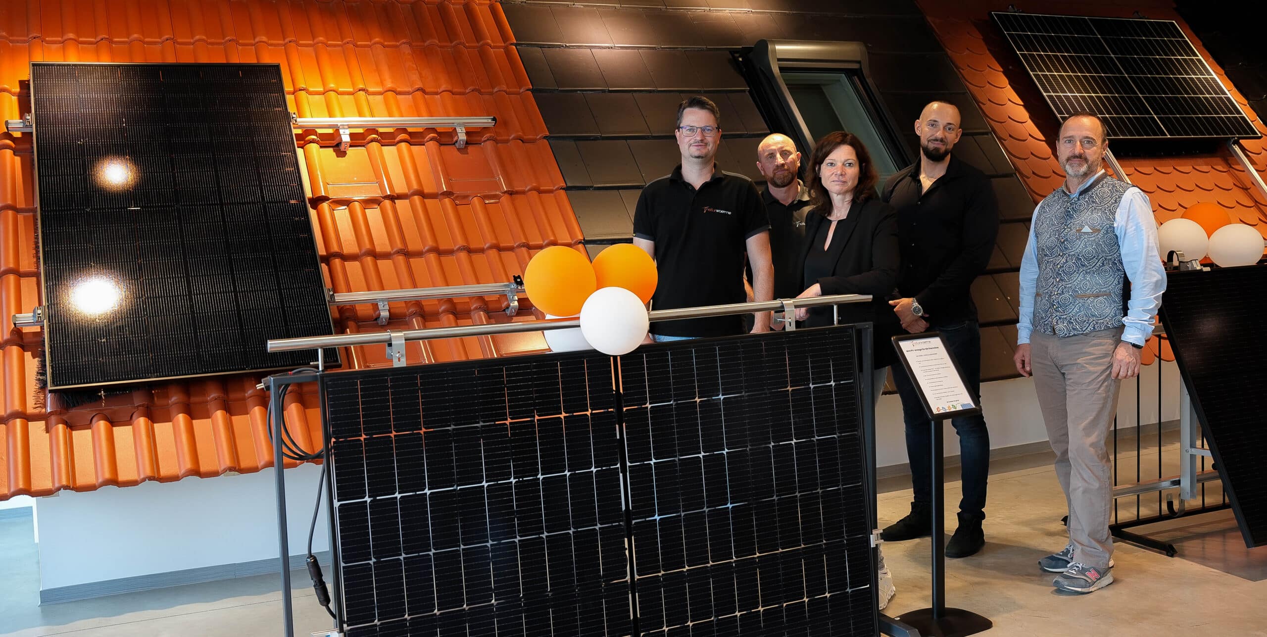 Vier Männer und eine Frau stehen vor einem Musterdach in der Photovoltaik Ausstellung Bruchköbel.