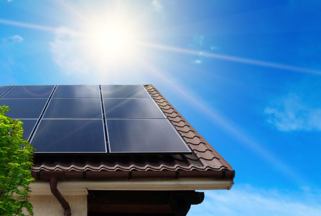 Hausdach mit Photovoltaikmodulen, strahlendem blauen Himmel und Sonne.