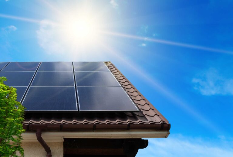 Hausdach mit Photovoltaikmodulen, strahlendem blauen Himmel und Sonne.