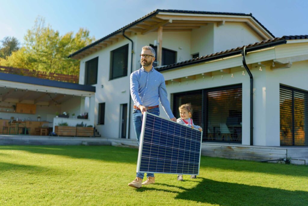 Vater und Tochter tragen Solarmodul im Garten
