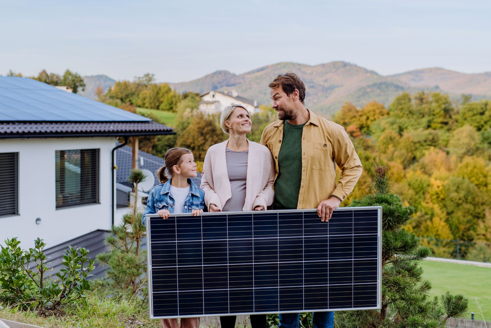Familie mit Solarmodul vor Haus