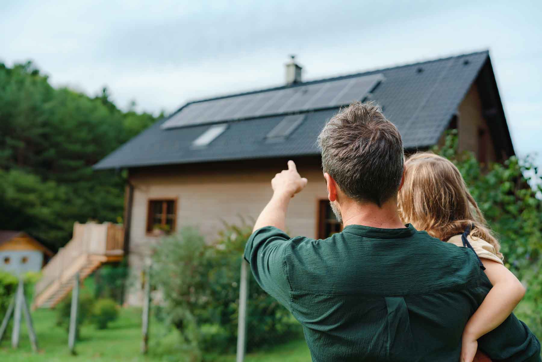 Vater mit Kind auf dem Arm vor einem Haus mit Photovoltaikanlage