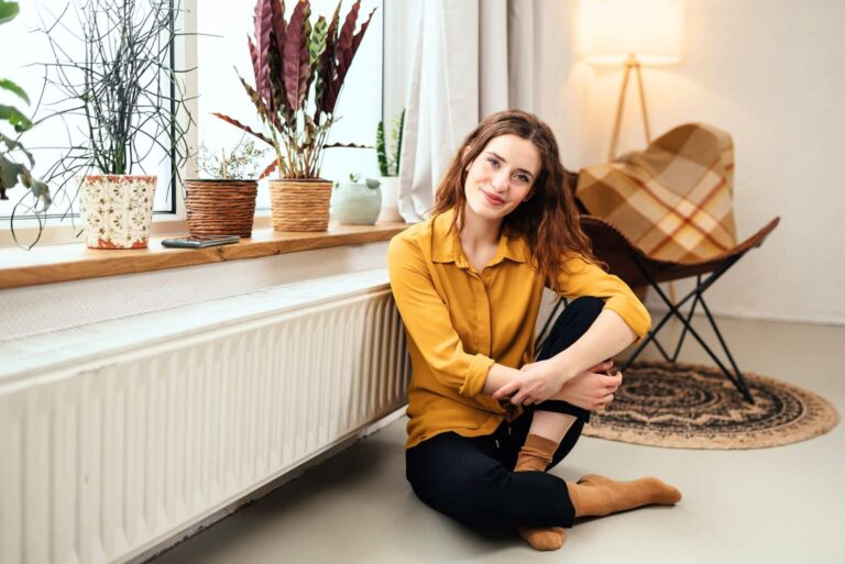 Frau sitzt vor Heizkörper