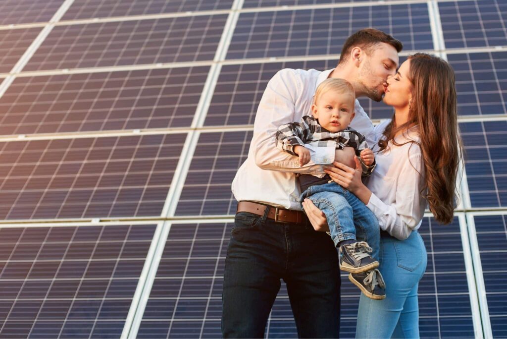 Paar mit Kleinkind küssen sich vor Solarmodulen, Symbolbild PV-Anlage anmelden
